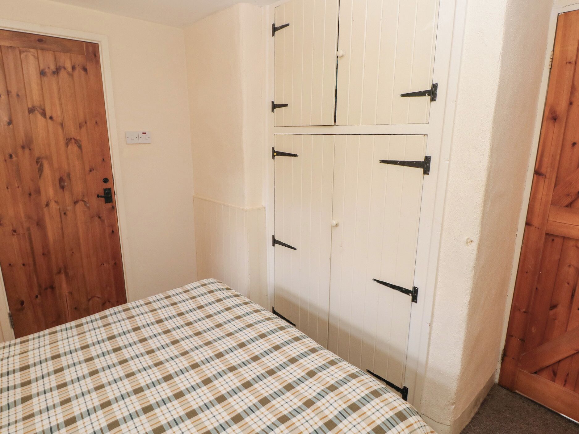 A bedroom with a wooden door, a bed with a plaid bedspread, and a white wardrobe with black handles.