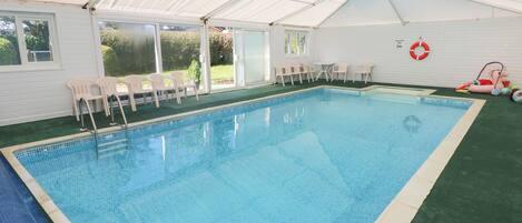 An indoor swimming pool with clear blue water, surrounded by white walls and a white roof.