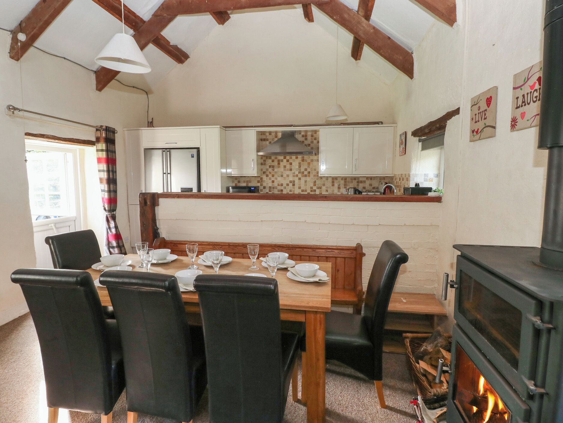 A dining area with a wooden table, black chairs, and a kitchen in the background.