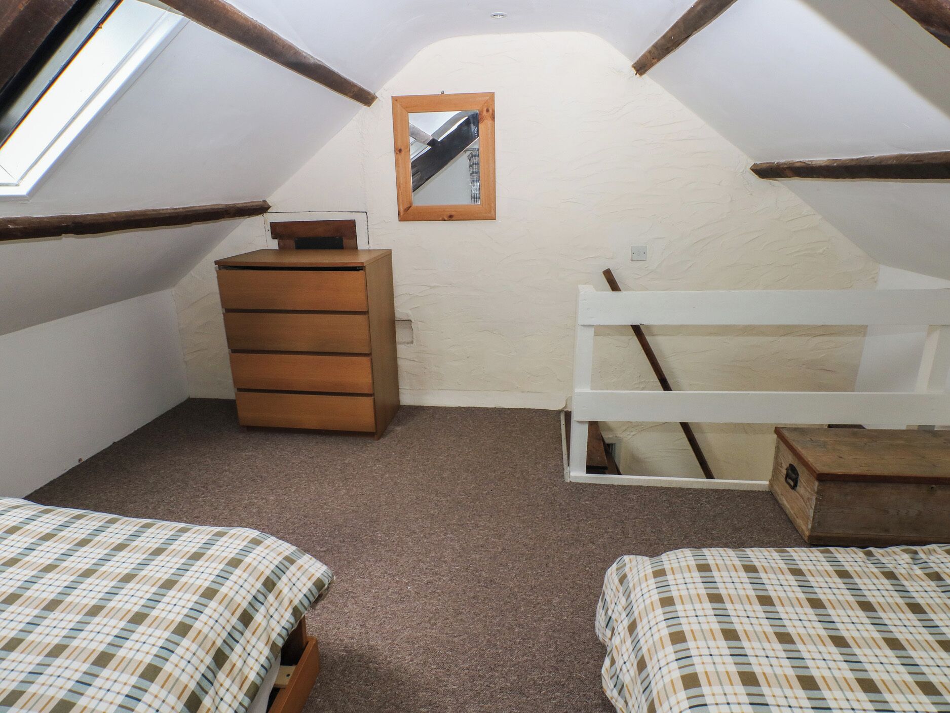A small, cozy attic bedroom with two beds, a wooden dresser, and a mirror on the wall.