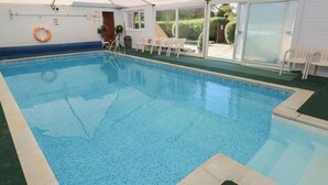 Ein Hallenbad mit klarem Wasser, umgeben von einem überdachten Bereich mit Liegestühlen und einem Rettungsring.