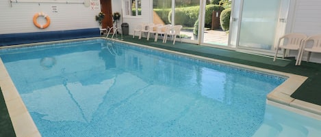An indoor swimming pool with clear water, surrounded by a covered area with chairs and a lifebuoy.