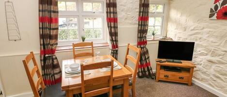 A cozy dining area with a wooden table and chairs, a television on a wooden stand, and a window with curtains.