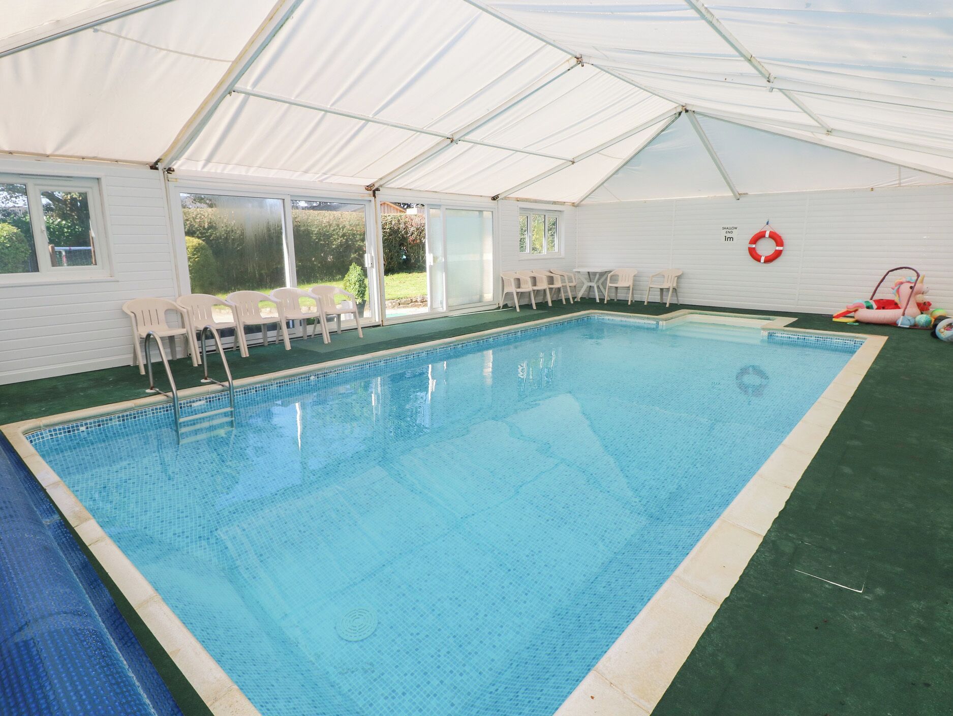 Una piscina interior con agua azul cristalina, rodeada de paredes y techo blancos.