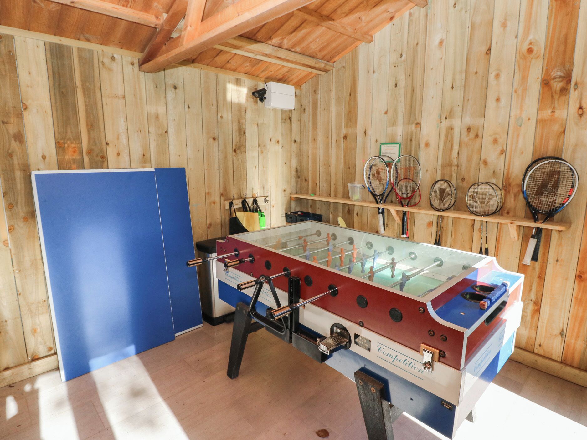 A foosball table in a wooden room with tennis rackets on the wall.