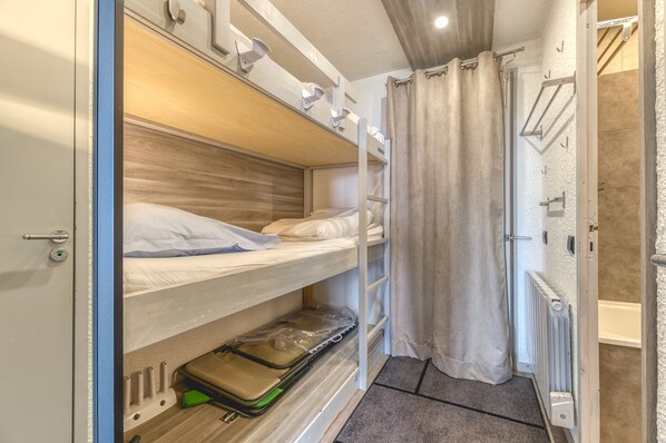 A bunk bed with a suitcase under the lower bunk, a radiator, and a shower area with a curtain.