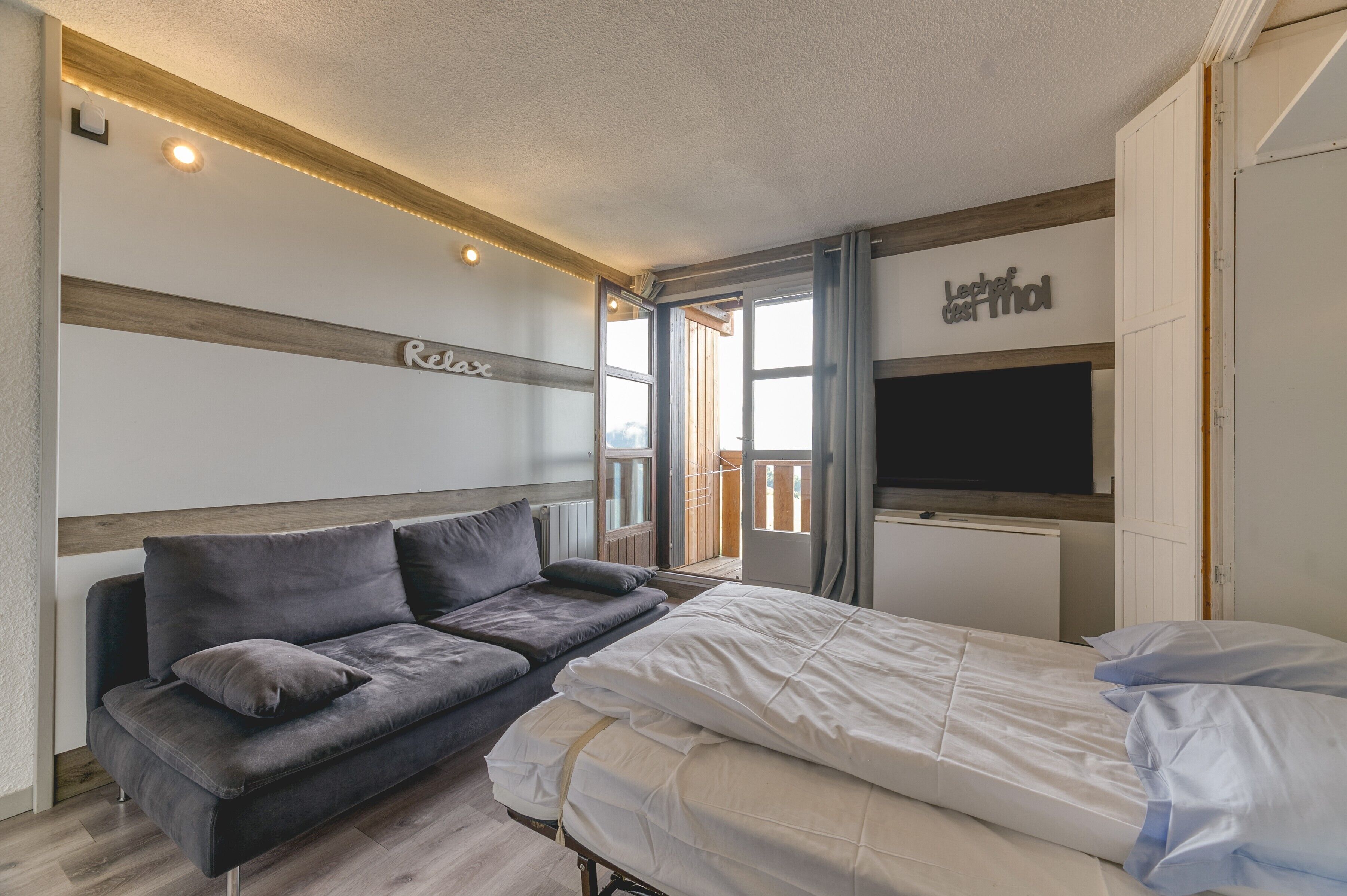 Et soveværelse med seng, sofa, fjernsyn og balkon.