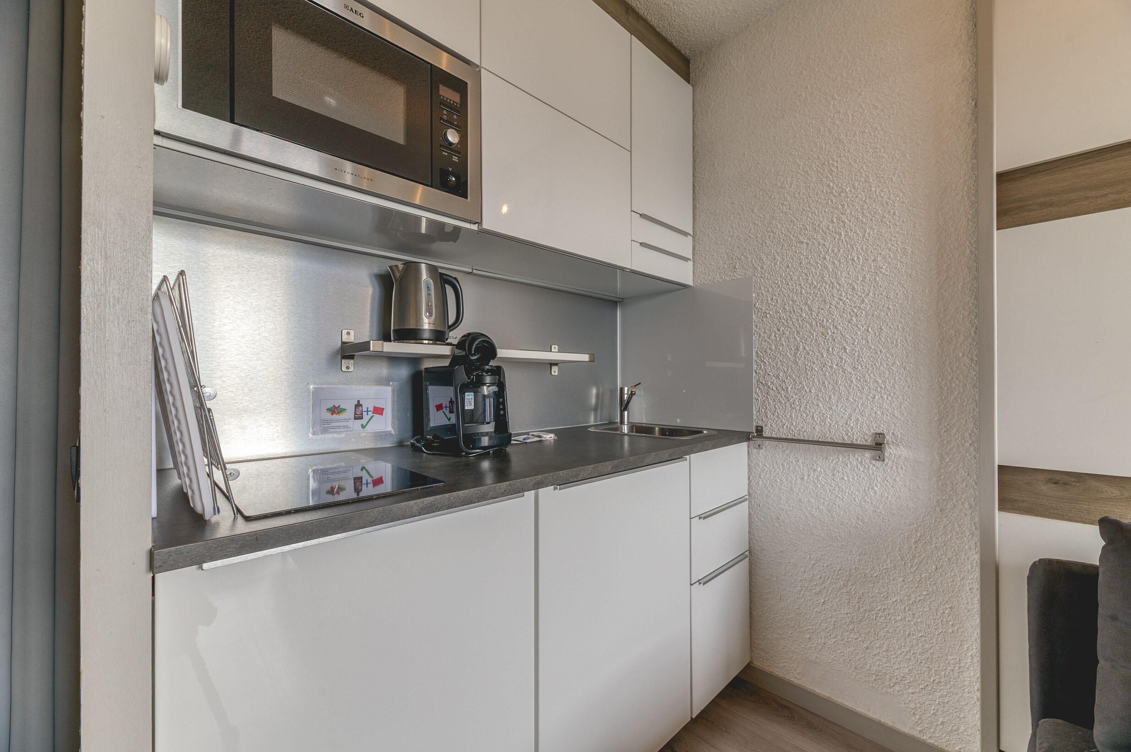 Een kleine keuken met een magnetron, koffiezetapparaat en waterkoker op het aanrecht.
