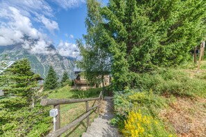 A mountain lodge with a wooden staircase, surrounded by dense forest and mountains.