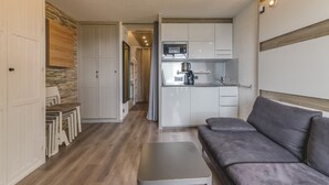 Een compacte leefruimte met een kitchenette, een bank, een eettafel met stoelen en een kledingkast.