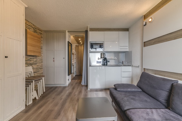 Un espacio habitable compacto con kitchenette, un sofá, una mesa de comedor con sillas y un armario.