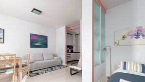 Une chambre d’hôtel moderne comprenant un lit, un canapé, une table à manger avec des chaises, un coin cuisine et des œuvres d’art accrochées aux murs.