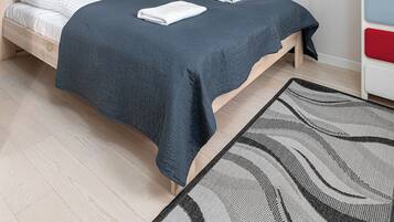 Un lit bien fait, recouvert d’une couvre-lit bleu foncé et agrémenté de deux serviettes blanches pliées, un plancher en bois, un tapis à motifs et deux œuvres d’art encadrées accrochées au mur.