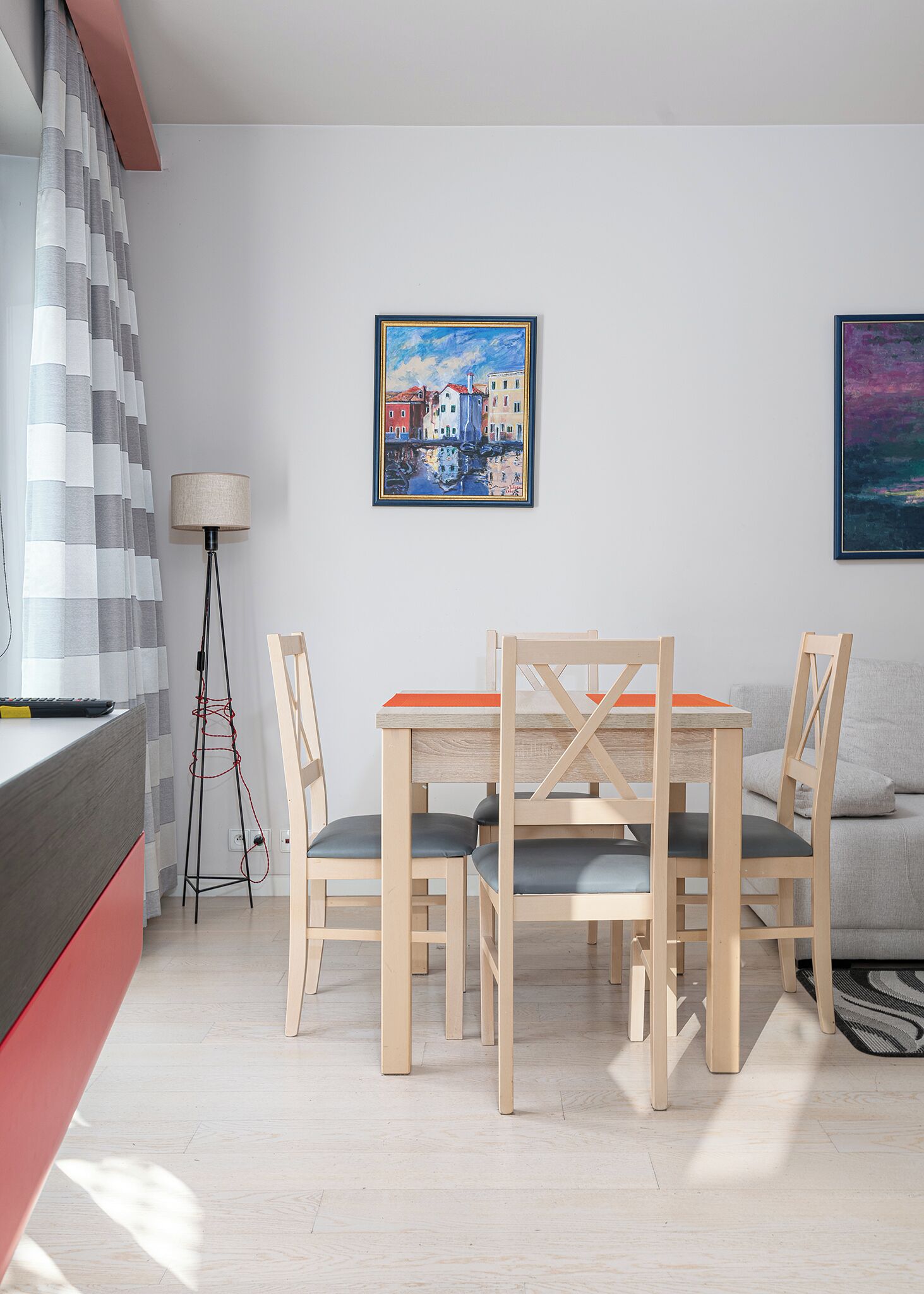 Una sala moderna con una mesa de comedor de madera y sillas, un sofá, una lámpara de pie y dos cuadros enmarcados en la pared.
