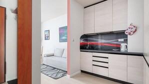 Une cuisine moderne avec des meubles de couleur bois clair, un plan de travail noir et une bouilloire rouge.