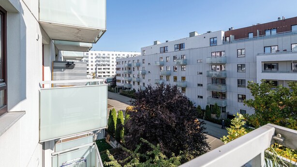 Un immeuble d’appartements moderne doté de balcons, un ciel dégagé et un arbre au premier plan.