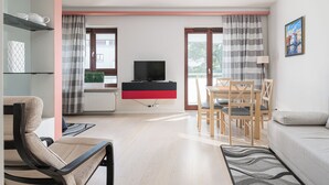 Un salon moderne comprenant un canapé, un téléviseur, une table à manger avec des chaises et un coin cuisine avec un réfrigérateur et un four à micro-ondes.