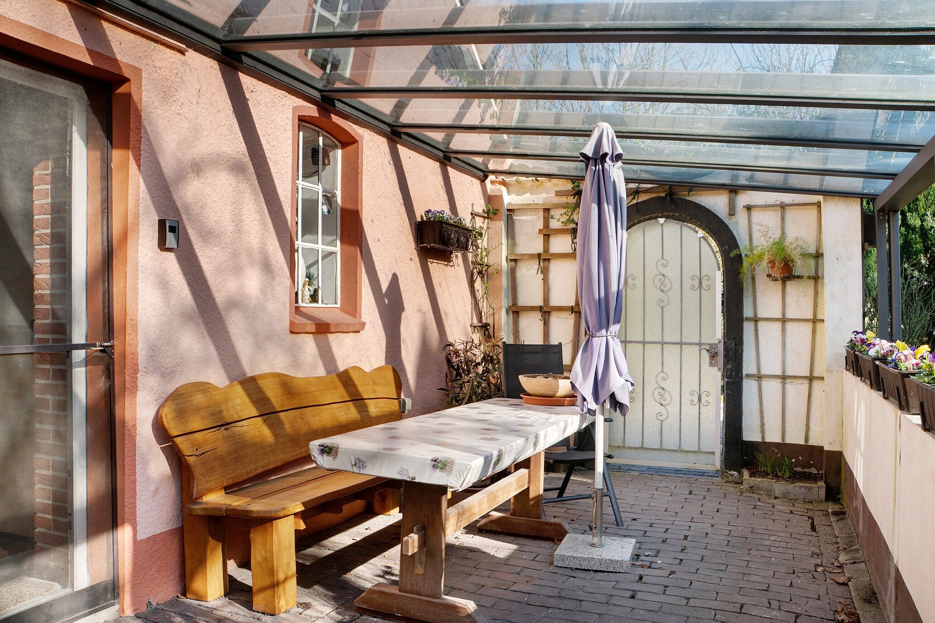 Eine überdachte Terrasse mit einer hölzernen Bank, einem Tisch und einem Blumentopf.