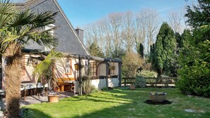 Una casa con un porche cubierto, césped y un jardín con diversas plantas y un bebedero para pájaros.