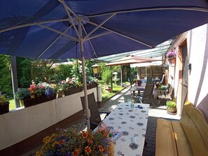 Eine Terrasse im Freien mit überdachter Sitzgruppe, einem Tisch und Stühlen sowie Pflanzen in Töpfen.