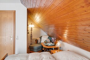 Ein gemütliches Schlafzimmer im Dachgeschoss mit geneigter Decke, einem Bett, einem kleinen Tisch mit Lampe und einem Sessel.
