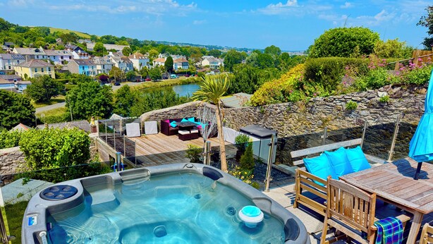 A hot tub with a wooden deck and outdoor furniture, overlooking a scenic village and greenery. - Cornish cottage.  Sleeps 8.  Dog friendly.  Lake views.  Close to the coast. (Millbrook)