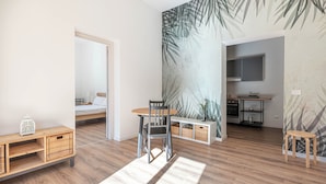 A modern room with a wooden floor, a dining table with chairs, a small kitchen area, and a bed with a white headboard. - Turati Apartment al Politeama by Wonderful Italy (Palermo)