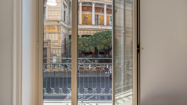 A view through a glass door with a decorative metal railing, leading to a street with pedestrians and a building with classical architecture. - Turati Apartment al Politeama by Wonderful Italy (Palermo)