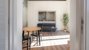 A modern kitchen with a dining area, featuring a wooden table, chairs, a grey sofa, and a large window with a view of the outdoors. - Turati Apartment al Politeama by Wonderful Italy (Palermo)