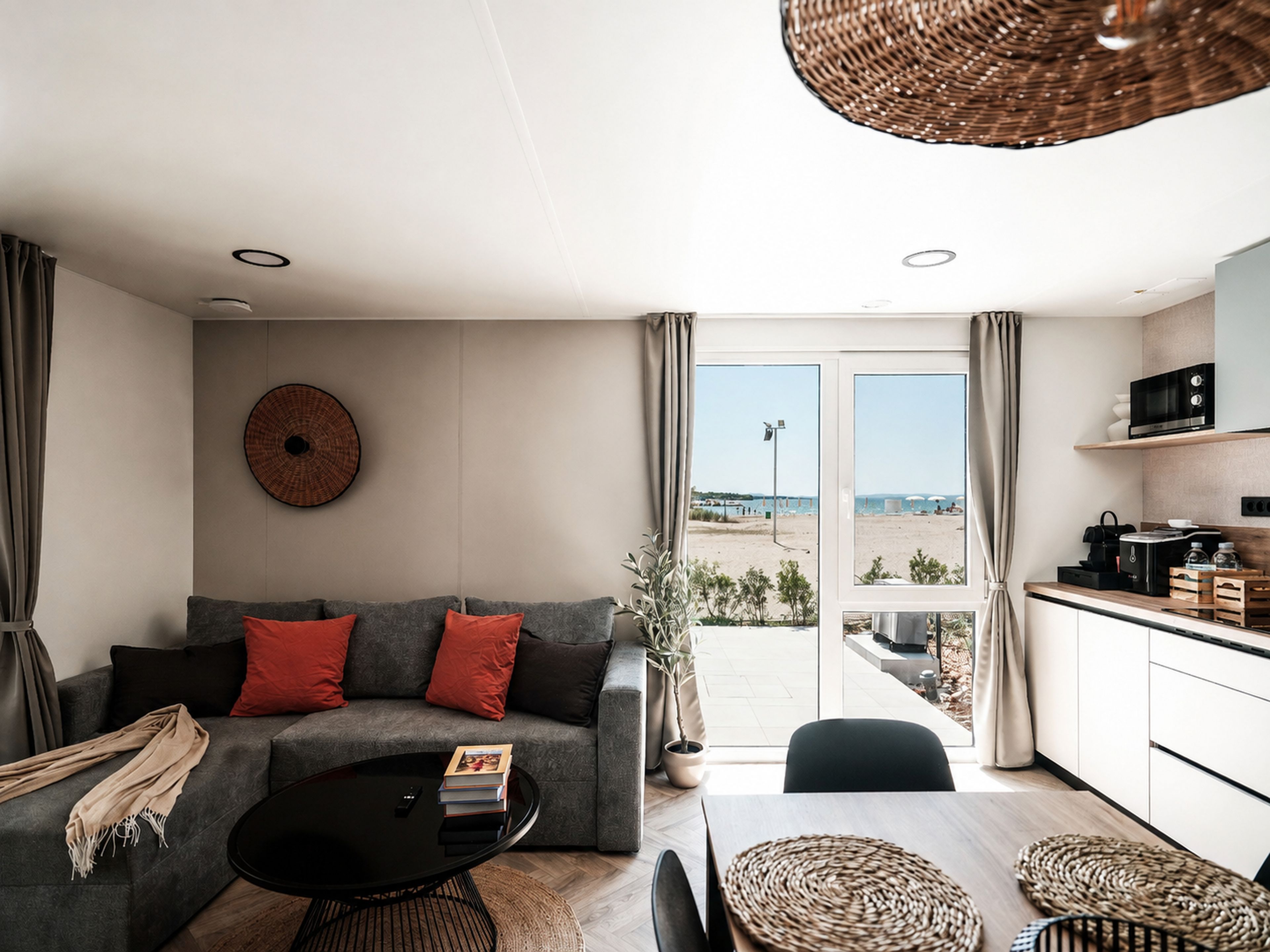 A modern living room with a sofa, coffee table, and a view of the beach through the glass door.