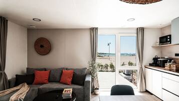 A modern living room with a sofa, coffee table, and a view of the beach through the glass door.