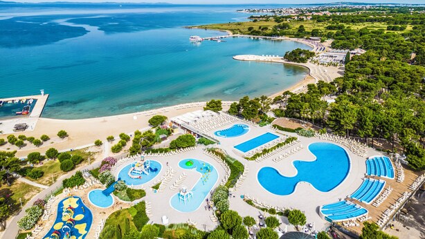 Vue aérienne d’une station balnéaire dotée de plusieurs piscines, d’une plage et d’un port de plaisance.