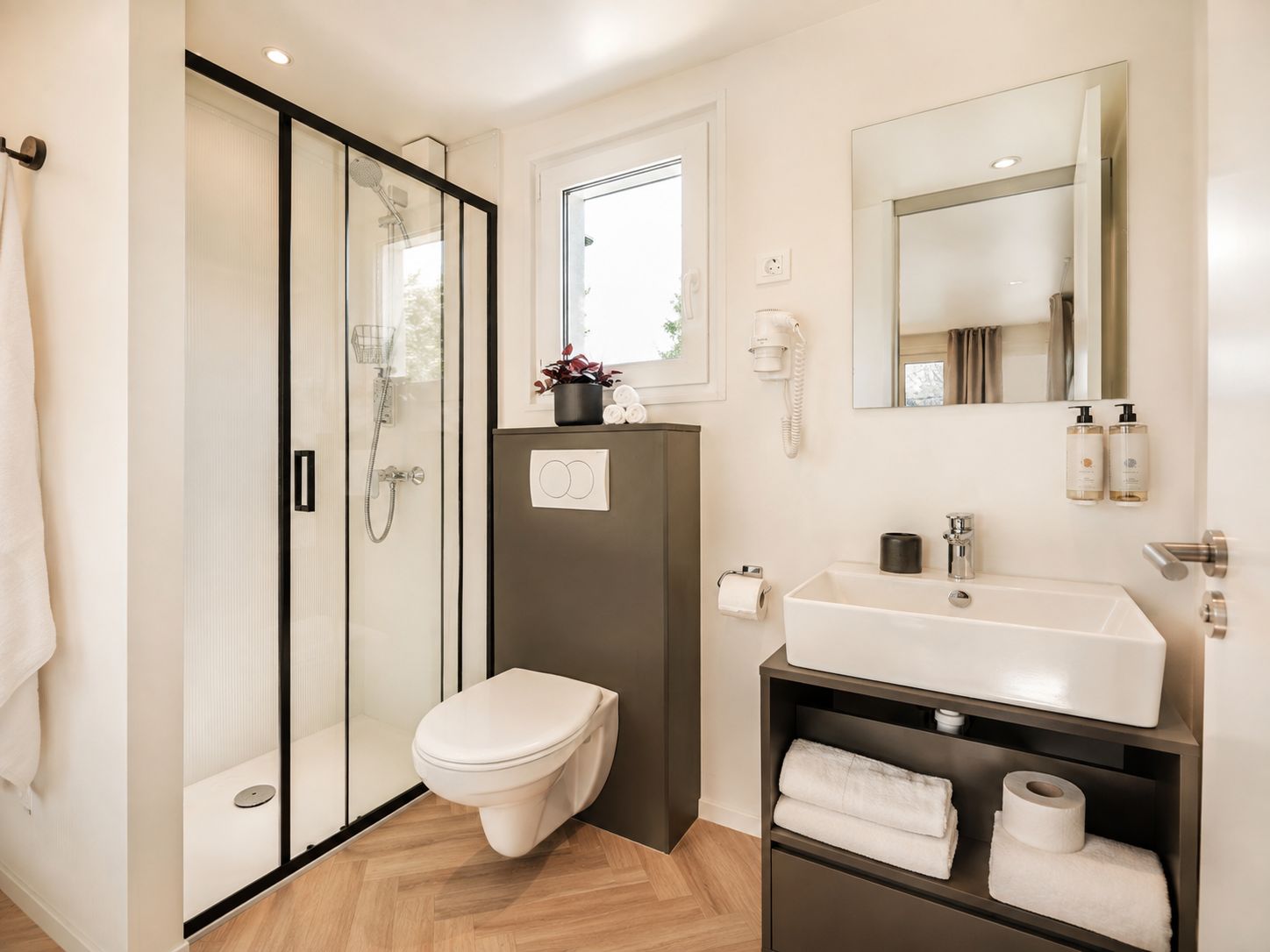 Un baño moderno con cabina de ducha de vidrio, inodoro, lavamanos con espejo y repisa con toallas.
