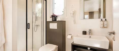 Un baño moderno con cabina de ducha de vidrio, inodoro, lavamanos con espejo y repisa con toallas.