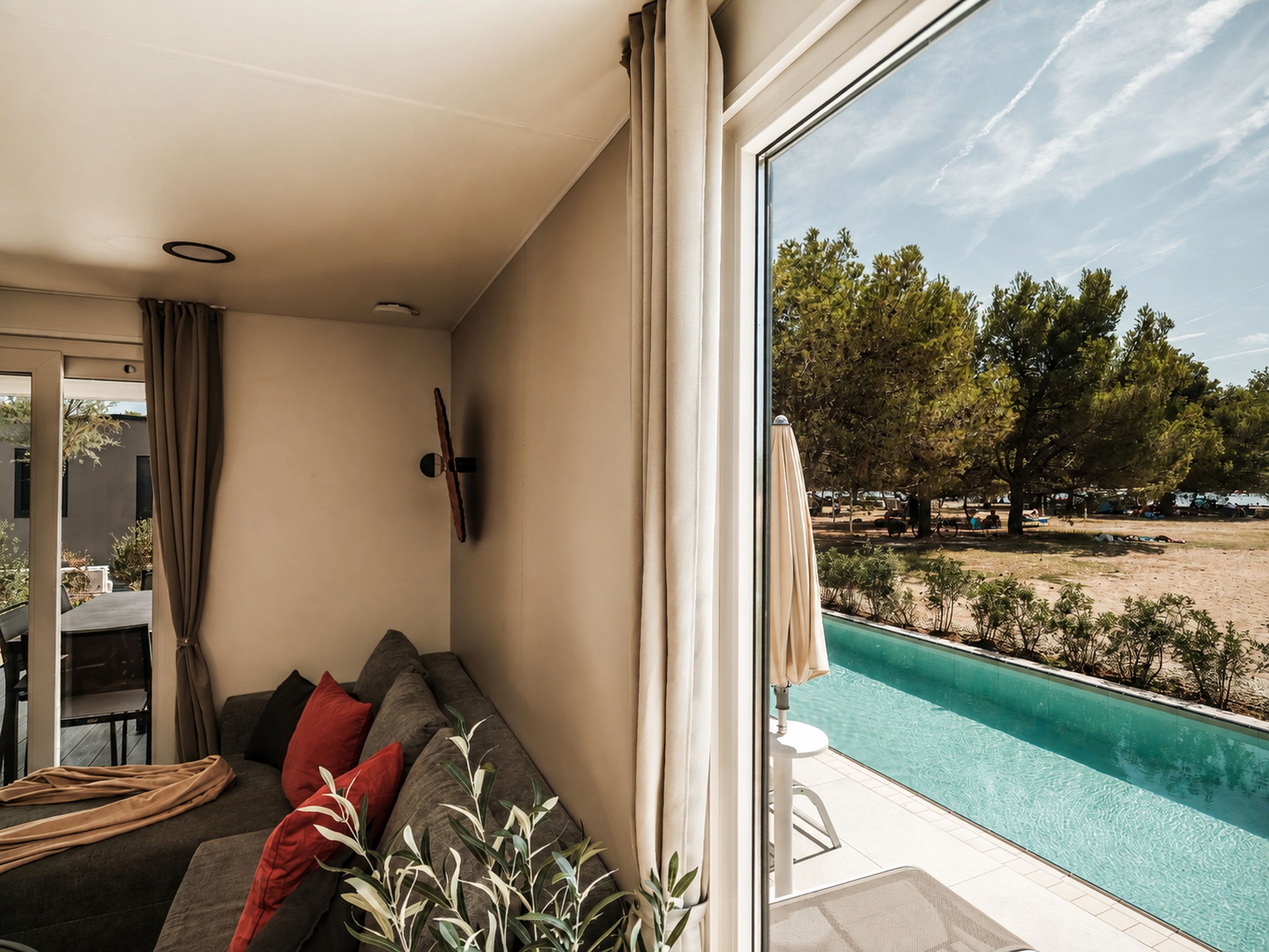 A modern living room with a large window overlooking a swimming pool and a beach.