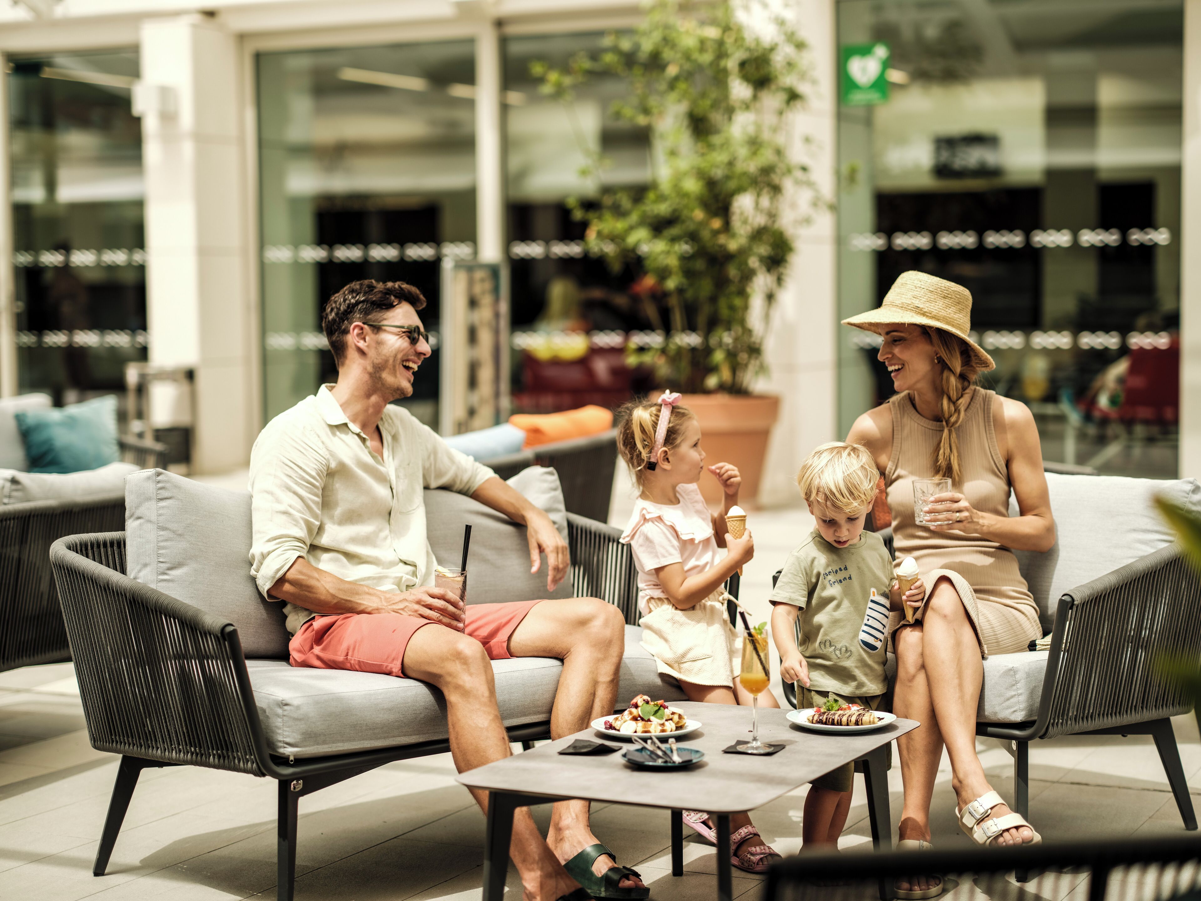 Eine Familie isst draußen auf einer modernen Terrasse mit Korbmöbeln und einem kleinen Tisch.