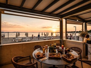 An outdoor dining area with a view of the sunset over the sea, tables set with food and drinks, and beach umbrellas. - Zaton Holiday Resort Glamping Village (Zaton)