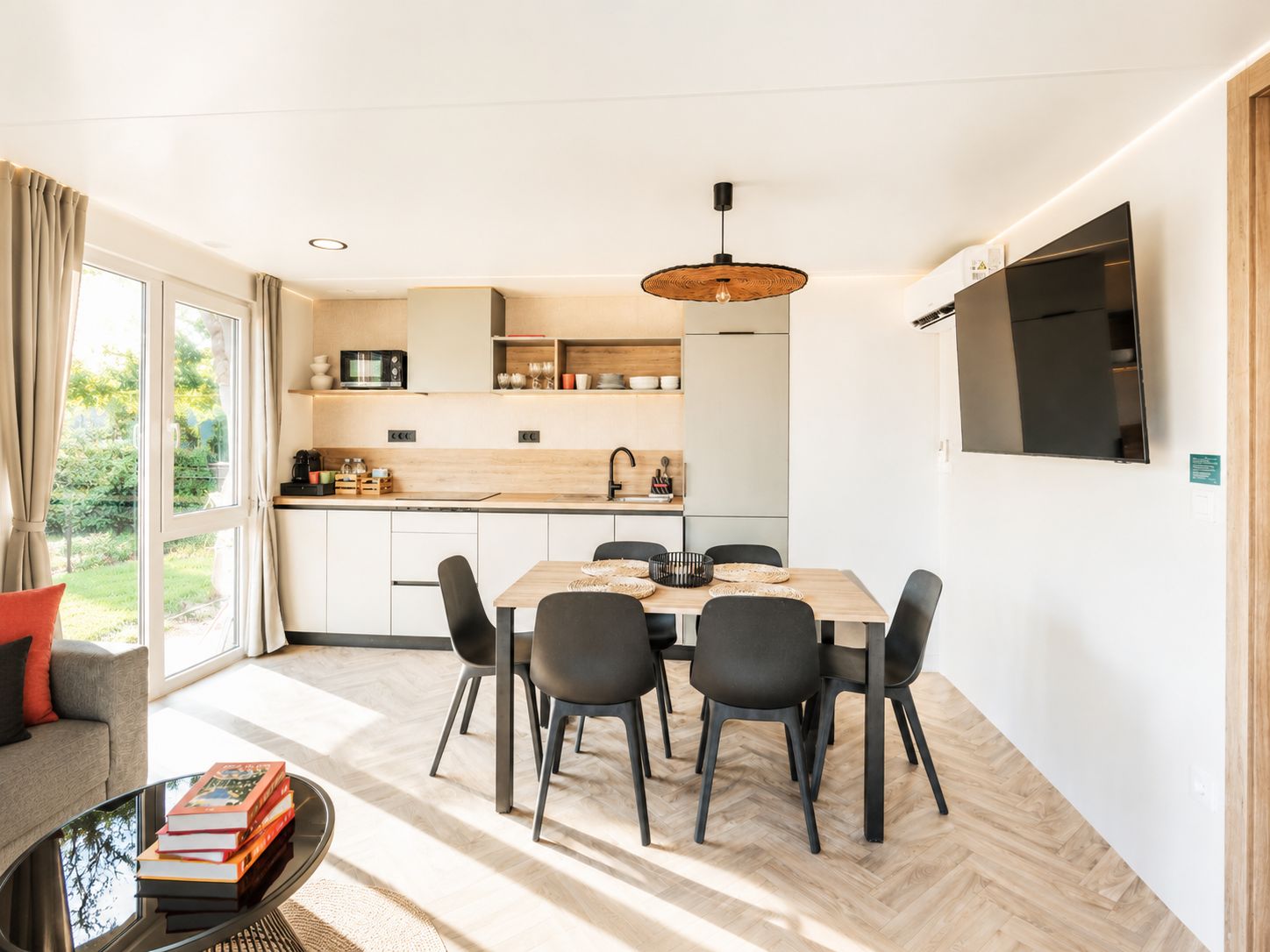 A modern kitchen with a dining area, large windows, and a flat-screen TV.