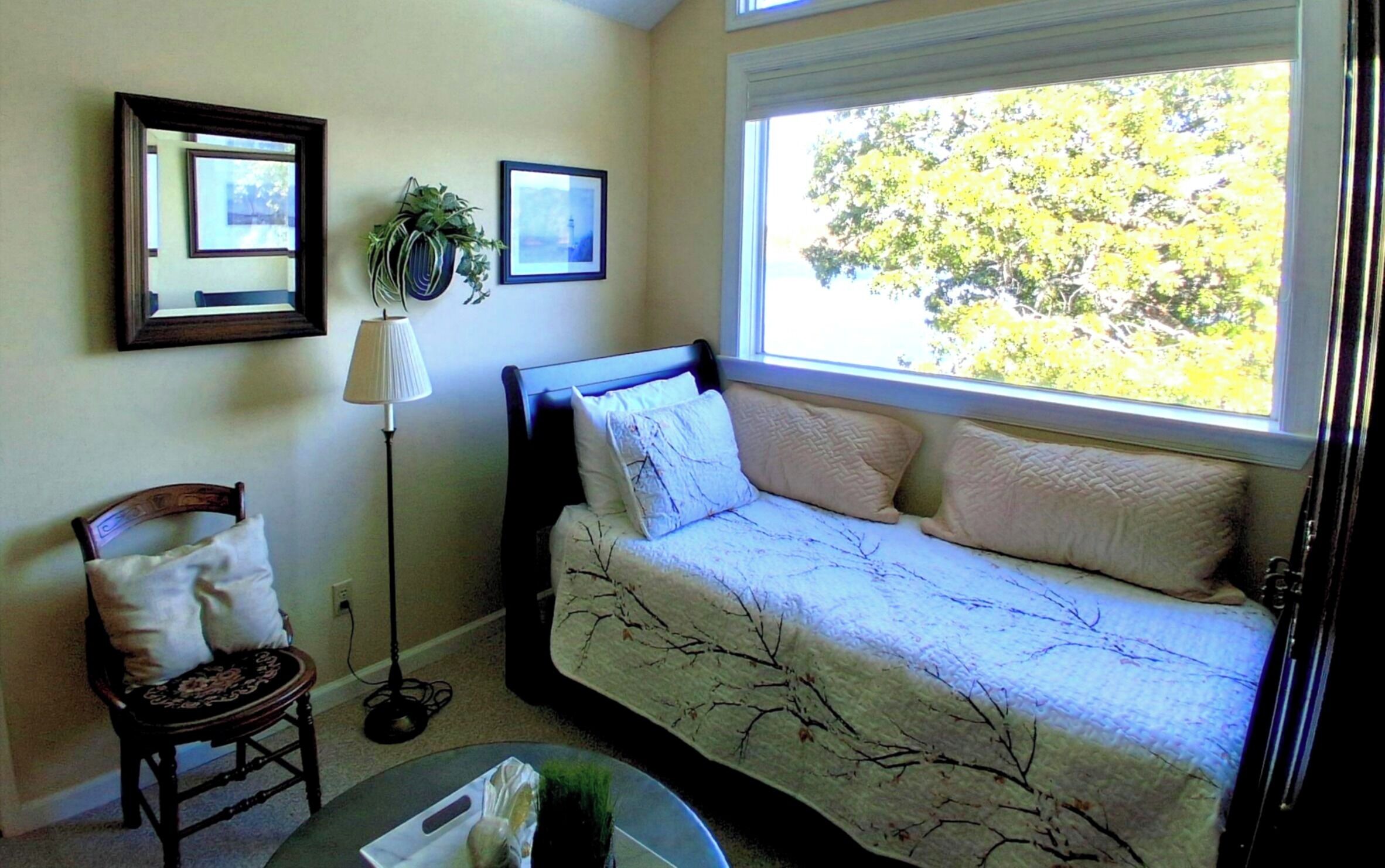 A bedroom with a bed, a chair, a floor lamp, and a window with a view of trees.