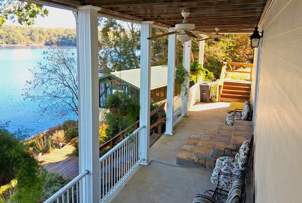 Eine überdachte Veranda mit Seeblick, Steintreppe und Gartenmöbeln.
