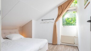 Ein Schlafzimmer mit Bett, Heizkörper, einem Fenster mit Vorhängen und einer Pendelleuchte.