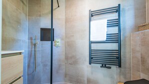Ein modernes Badezimmer mit Duschkabine aus Glas, einem schwarzen Handtuchhalter und einem Holzwaschtisch.