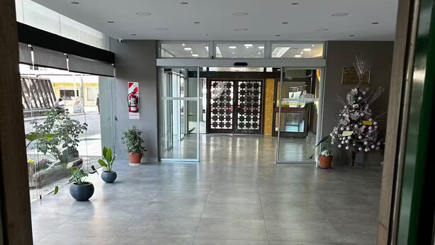 A modern hotel lobby with a tiled floor, glass doors leading to the reception area, and potted plants. - Entire condo in San Carlos de Bariloche, Argentina (San Carlos de Bariloche)