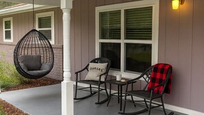 Een overdekt terras met buitenmeubels, waaronder een hangstoel, schommelstoelen en een tafel.