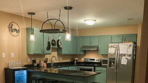 Een moderne keuken met blauwgroene kastjes, een centraal eiland met krukken, een koelkast en een kleine koelkast.