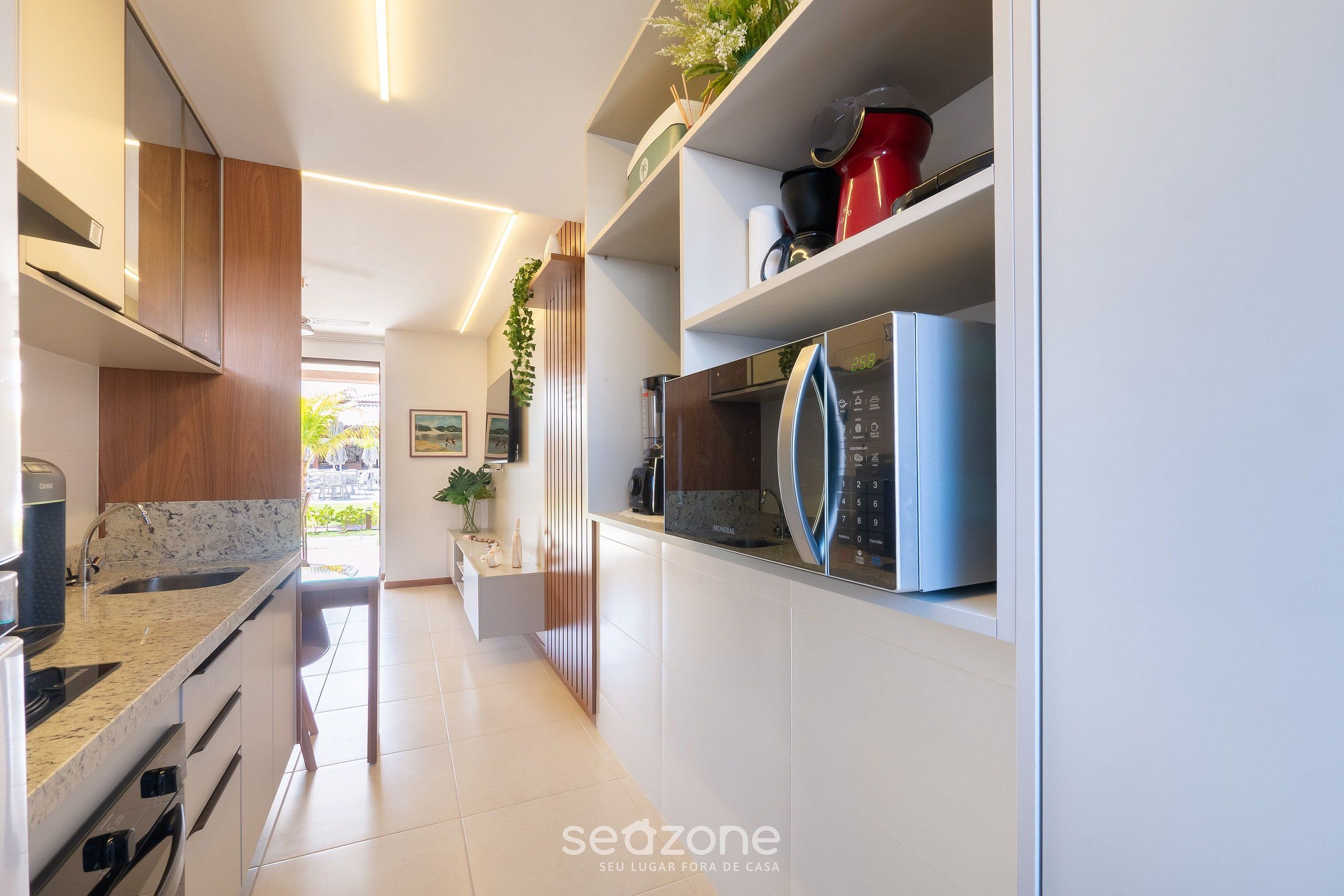 Una cocina moderna con armarios blancos, microondas integrado y cafetera.