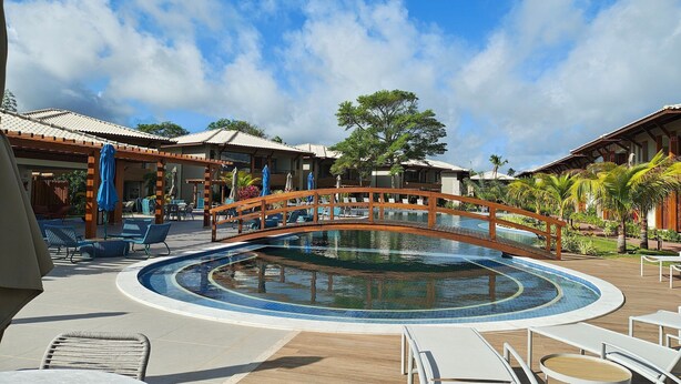 Area piscina di un resort con un ponte di legno, sdraio e ombrelloni.