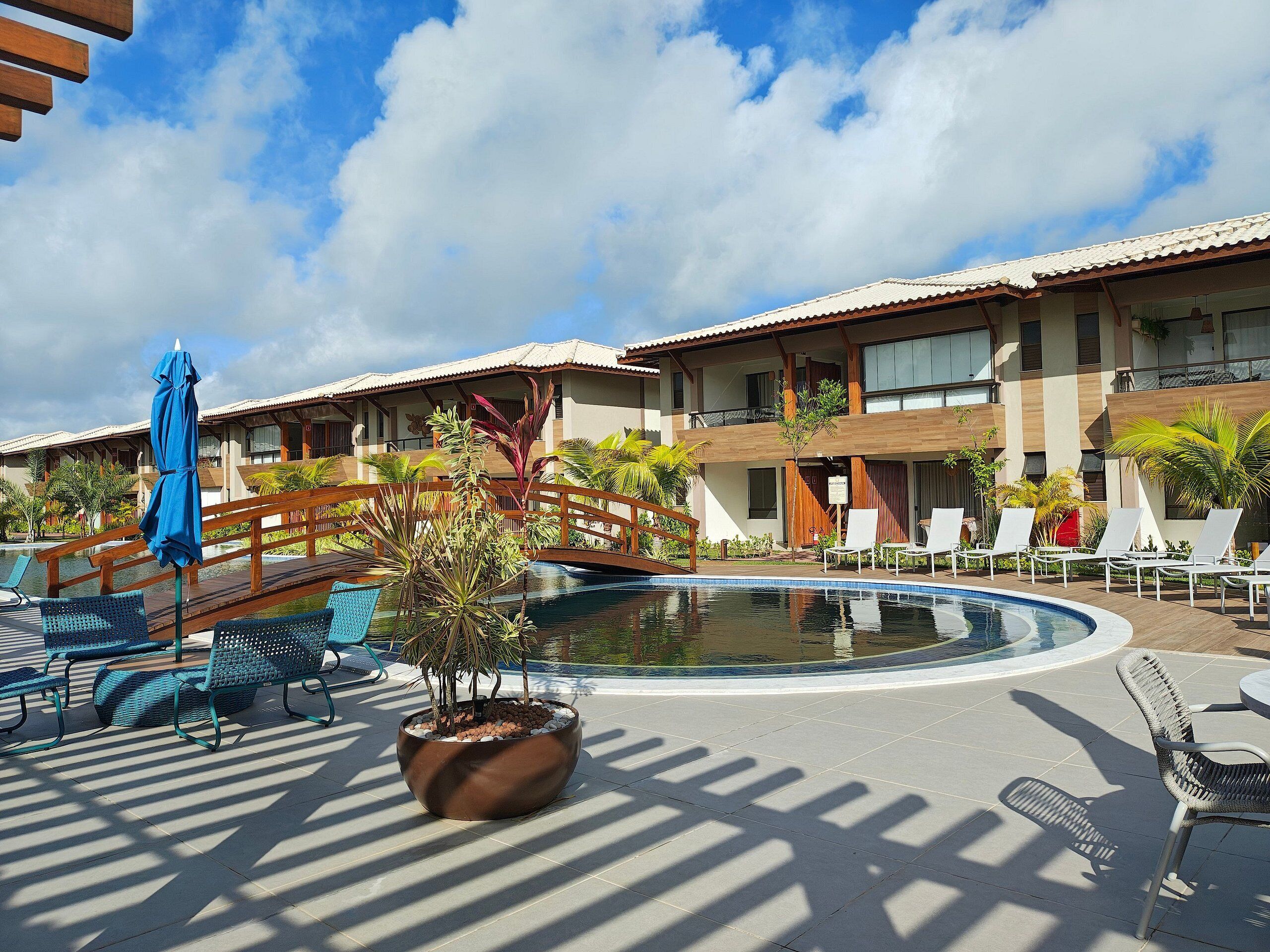 A resort pool area with lounge chairs, a small bridge, and a potted plant.
