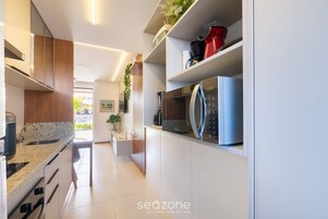 Cozinha moderna com armários brancos, micro-ondas embutido e máquina de café.