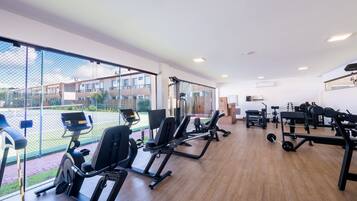 Uma academia com máquinas de cardio, equipamentos de musculação e uma grande janela com vista para um pátio.